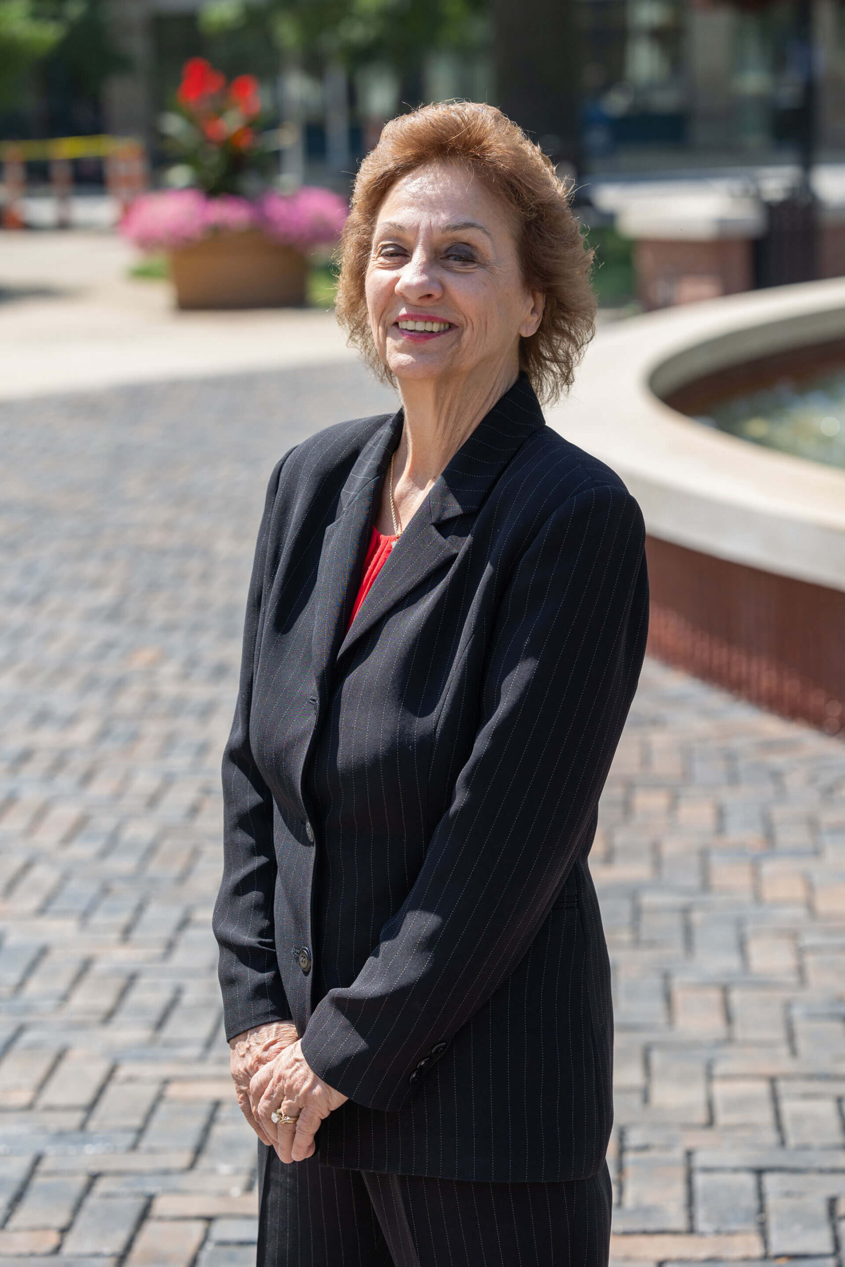 Priscilla Berthold smiling in front of a fountain and flowers