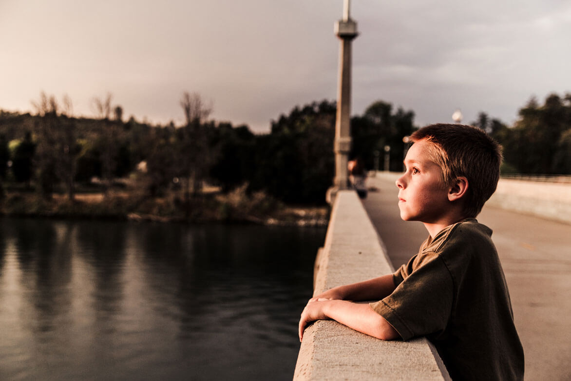 Child standing alone on bridge looking forlornly into the distance